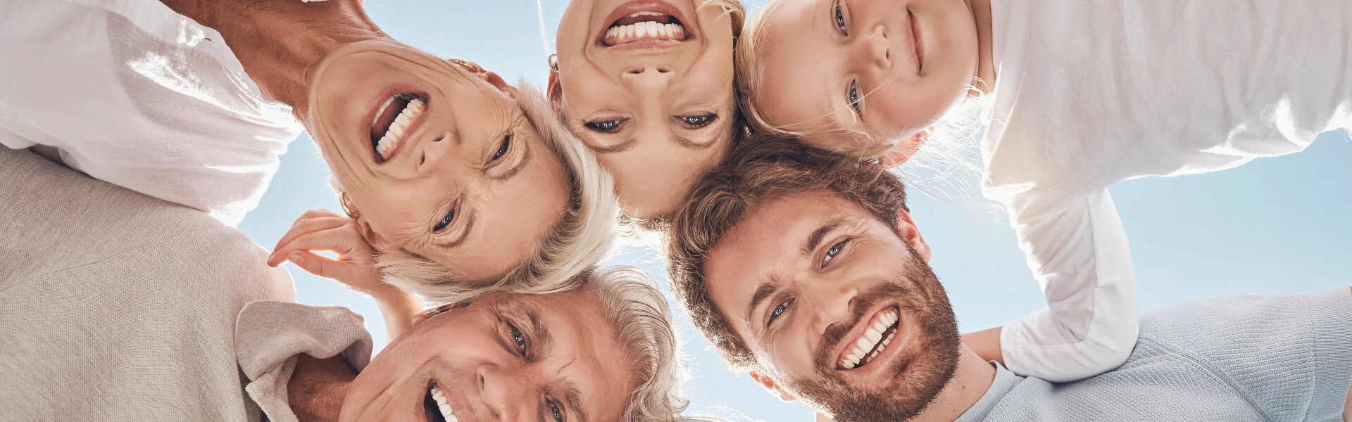 Mehrgenerationenfamilie lacht glücklich im Kreis unter blauem Himmel, Familienglück draußen.