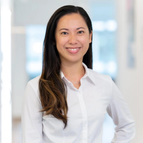 Junge Geschäftsfrau im weißen Hemd lächelt in modernem Büro mit hellen Hintergründen.